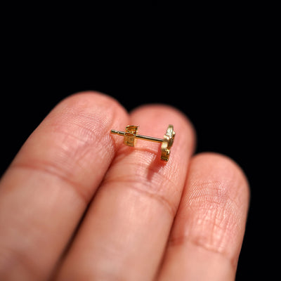 A 14k gold Diamond Evil Eye Earring sitting sideways on a model's fingertips to show detail