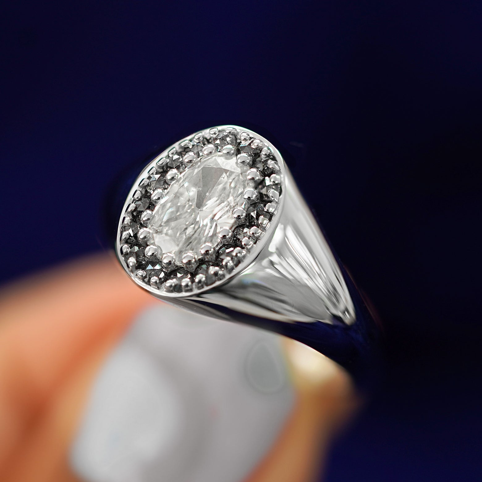 A model holding a diamond halo platinum signet ring between their fingertips to show the details of the ring face