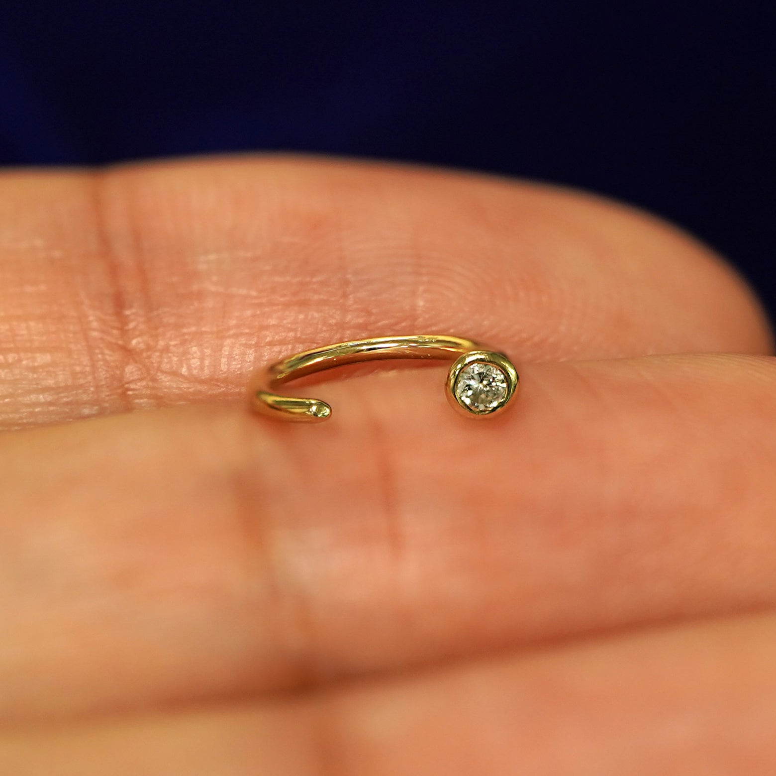 A 14k yellow gold Diamond Open Hoop resting on a models fingertip to show the open part of the earring
