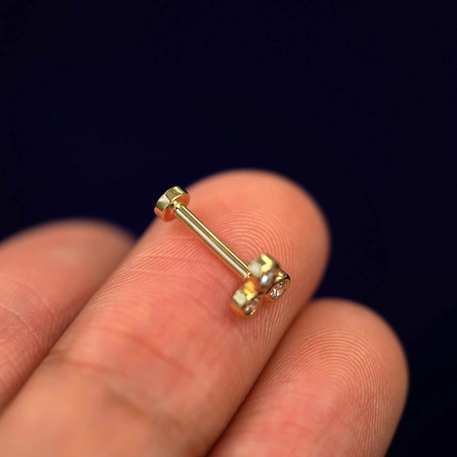 Alternate side view of a Diamond Trio flat back piercing sitting on a model's fingertips