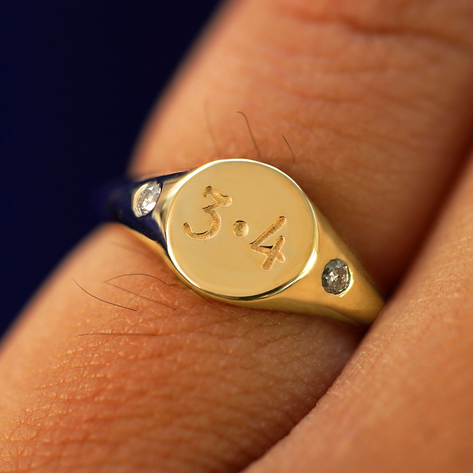 Close up view of a model's fingers wearing a yellow gold diamond Signet Ring with 3.4 engraved on the top