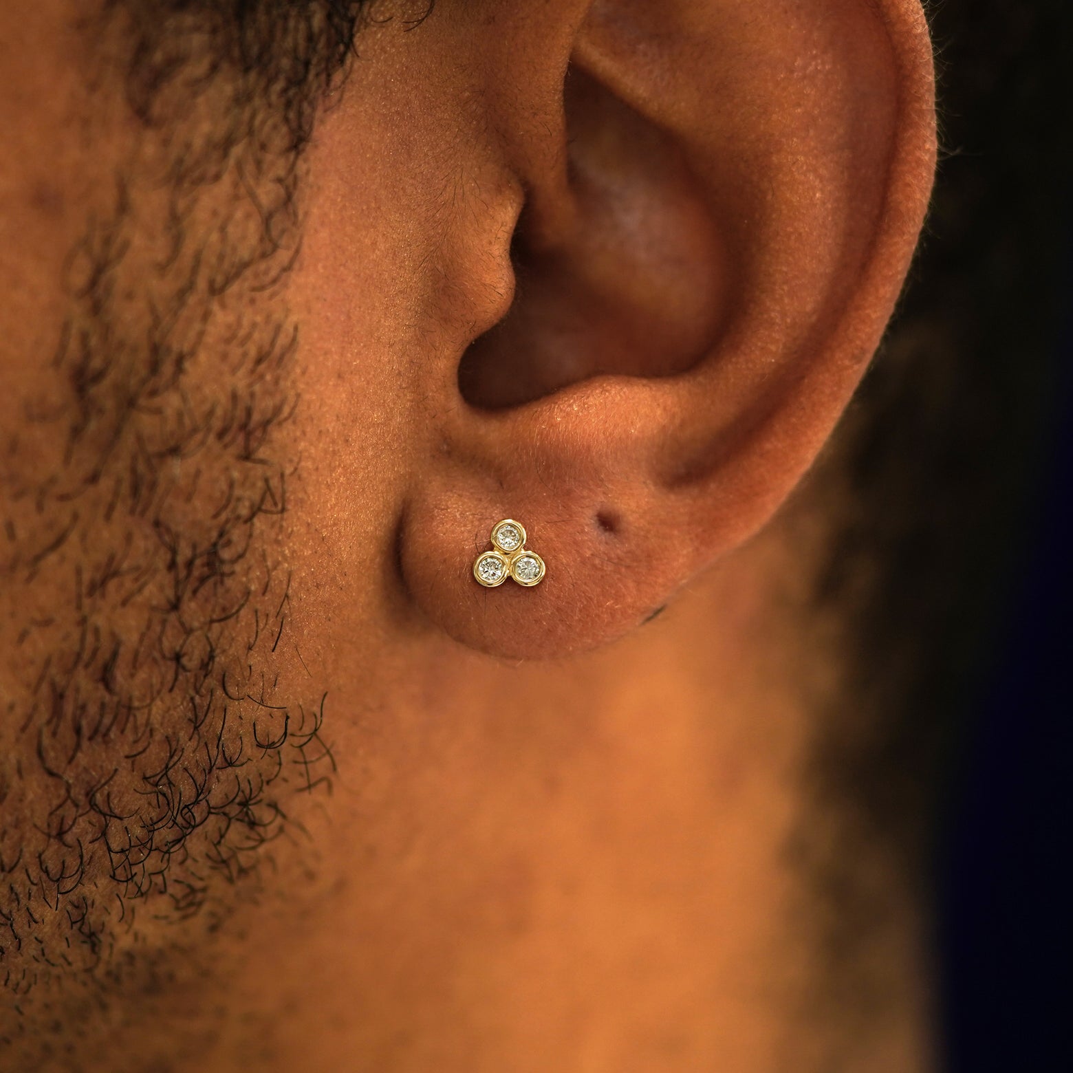 Close up view of a model's ear wearing a 14k yellow gold Diamond Trio Flatback Piercing