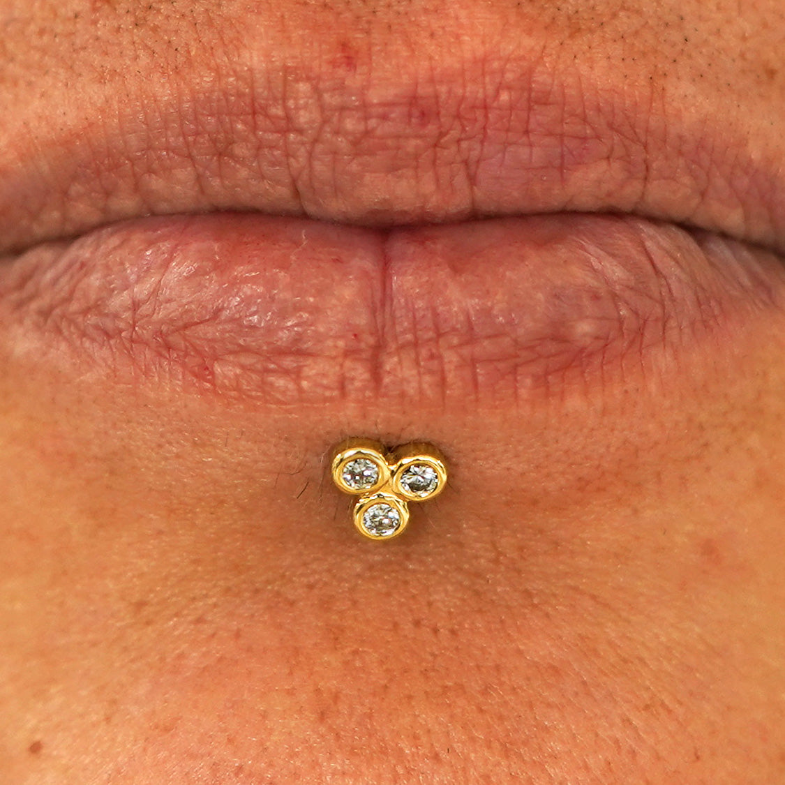 Close up view of a model's lips wearing a 14k yellow gold Diamond Trio Flatback in a labret piercing