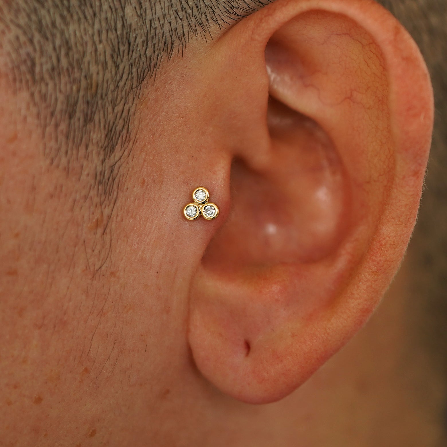 A model's ear wearing a 14k yellow gold Diamond Trio Flatback in a tragus piercing