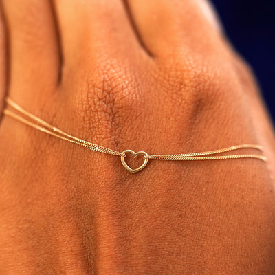 A solid gold Heart Bracelet resting on the back of a model's hand