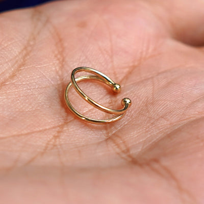 A solid yellow gold Double Cuff earring resting in a model's palm