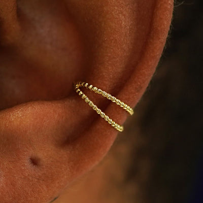 Close up view of a model's ear wearing a 14k yellow gold Bead Ear Cuff