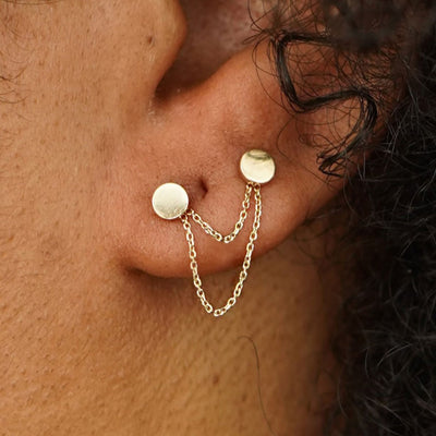 Close up view of a model's ear wearing two Circle Studs with a yellow gold Cable Chain Connector in front of their lobe