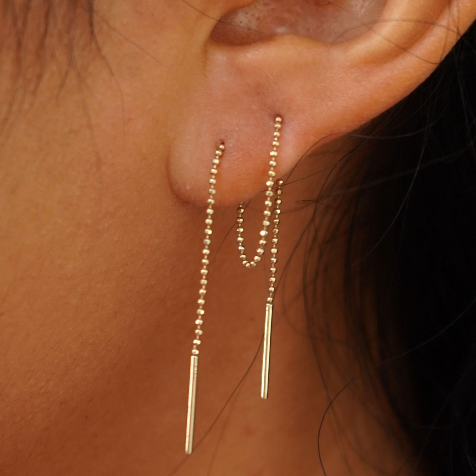 Close up view of a model's ear wearing a Threader through looped tightly in the front through two piercings and dangling