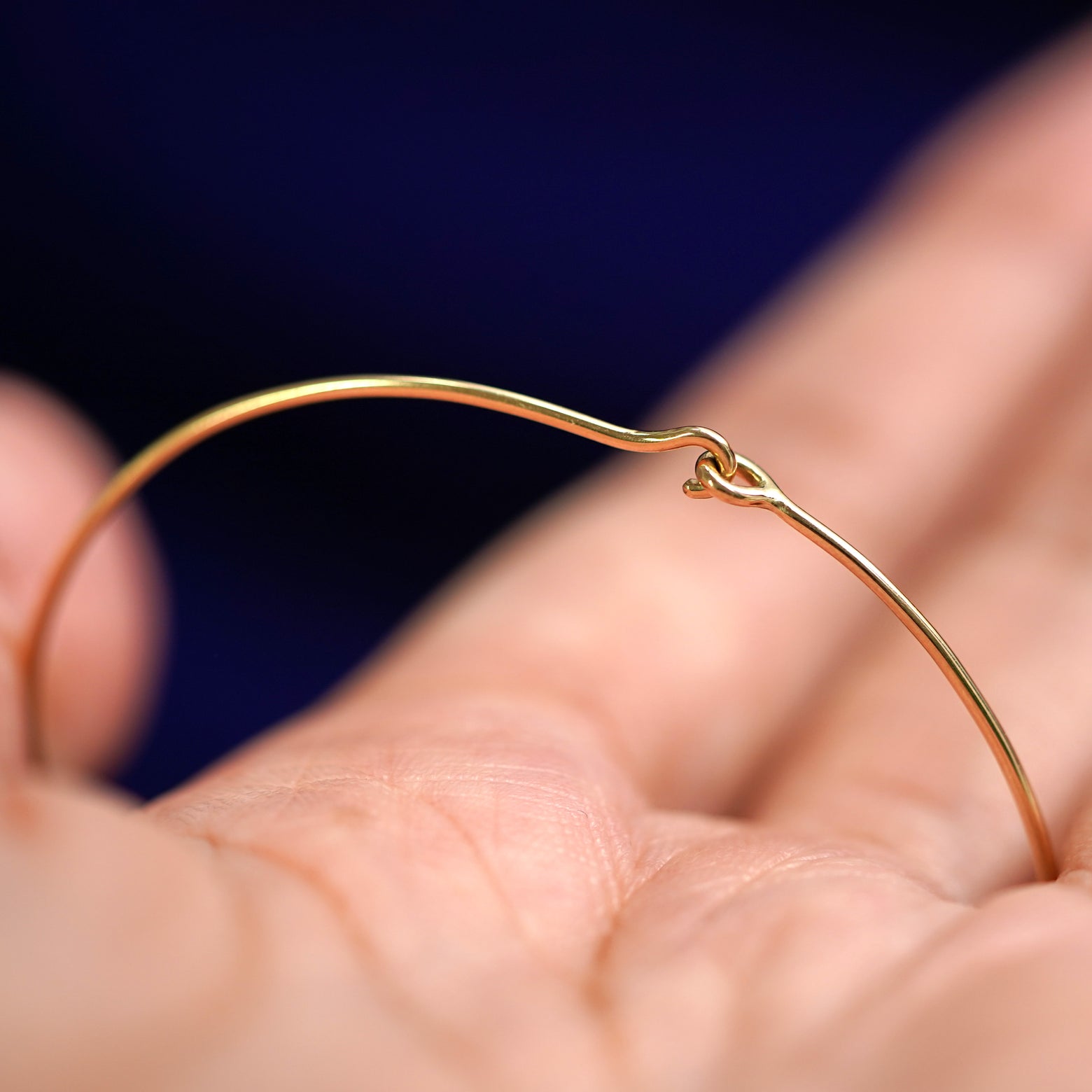 A model holding a 14k yellow gold Line Bangle Bracelet to show the easy hook clasp