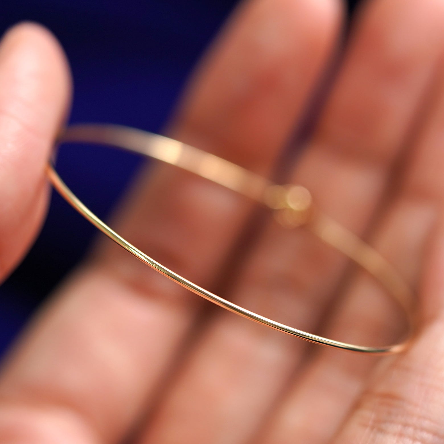 A yellow gold Line Bangle Bracelet held between a model's fingers