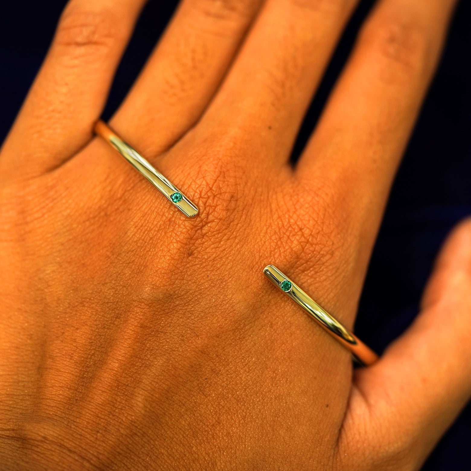 A solid gold emerald Gemstone Open Bangle Bracelet resting on the back of a model's hand