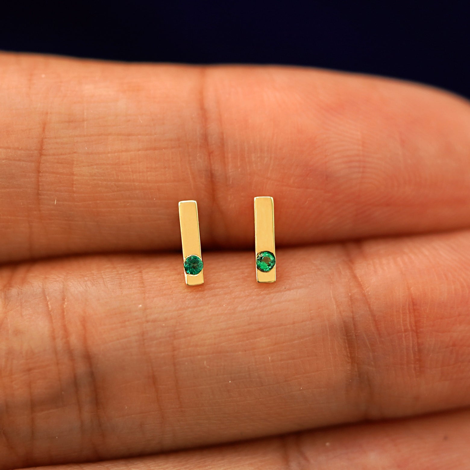 A model holding a pair of emerald Gemstone Bar Earrings in yellow gold between two fingers