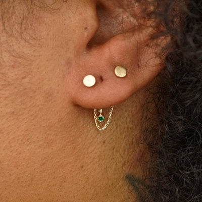 Close up view of a model's ear wearing a yellow gold emerald Cable Chain Connector across two Circle Studs behind their lobe