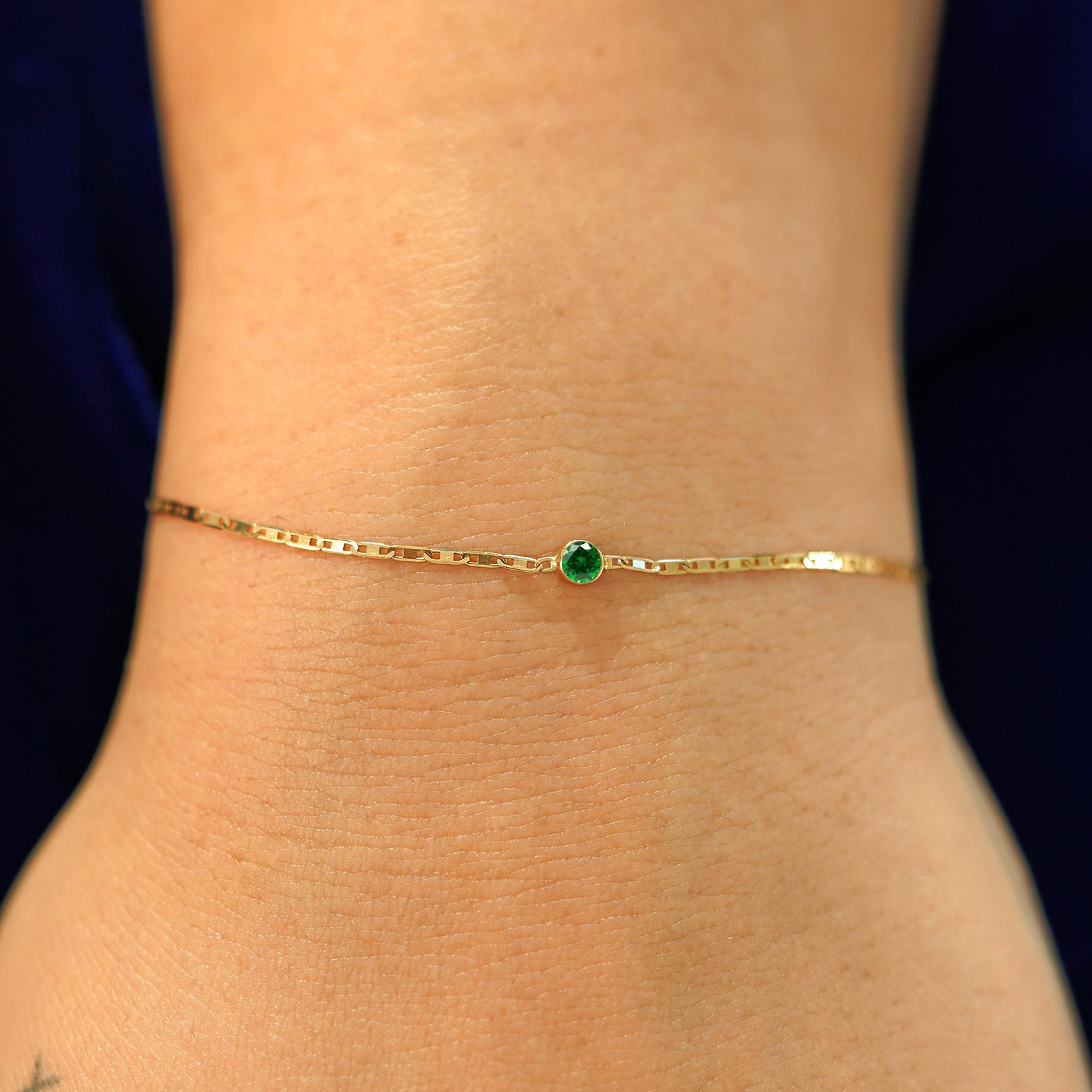 A model's wrist wearing a solid 14k yellow gold Emerald Bracelet