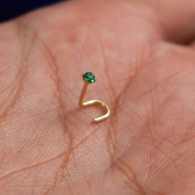 A 14 karat yellow gold Emerald Nose Stud standing upright to show detail and resting in the palm of a model's hand