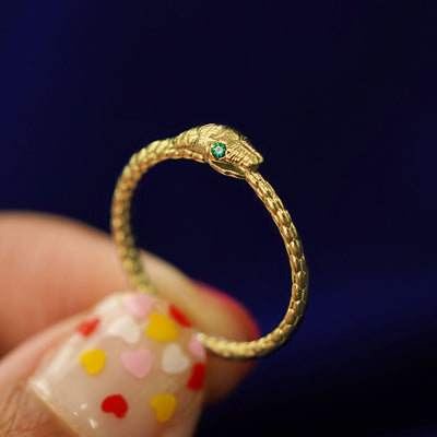 A model holding an emerald Ouroboros Snake Ring between their fingers to show the detail of the face and tail
