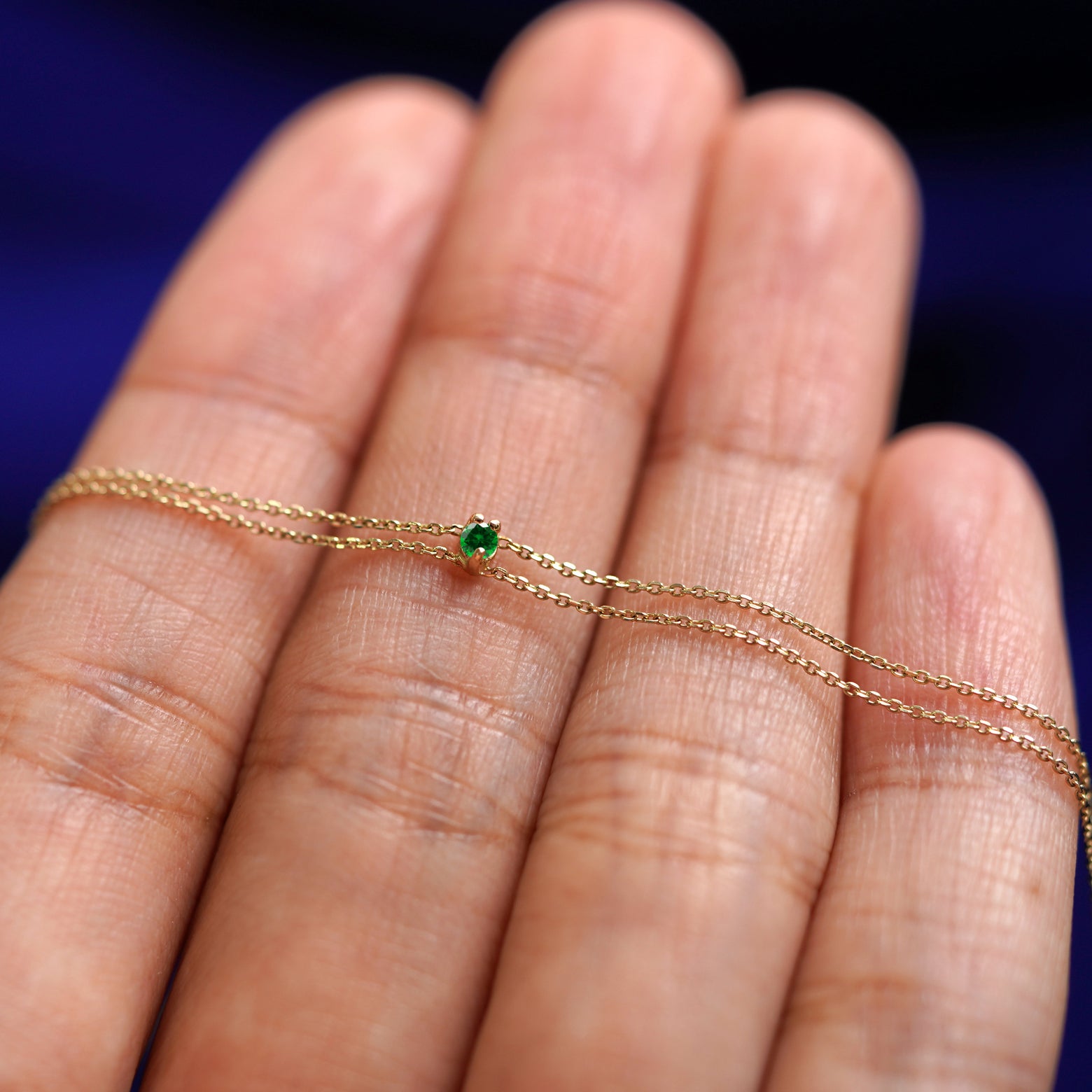 A yellow gold emerald Gemstone Cable Bracelet resting on a model's fingers