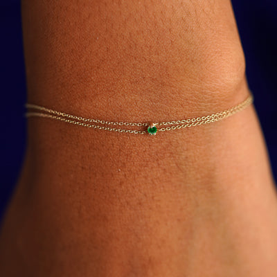 A model's wrist wearing a solid gold Gemstone Cable Bracelet in emerald