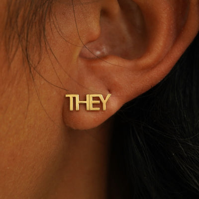 Close up view of a model's ear wearing a solid yellow gold They Earring