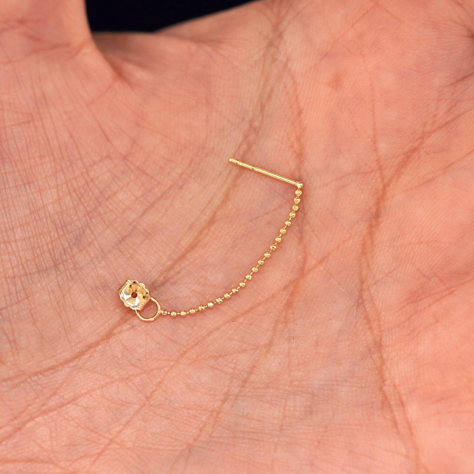 A solid yellow gold Chain Loop with the backing unattached to post sitting in a model's hand