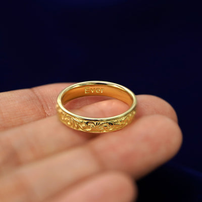 A Filigree Band resting on a model's fingertips to show the inside of band to be engraved with the word Ever