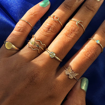 A model's hand lit by sunlight wearing various yellow gold Automic Gold rings
