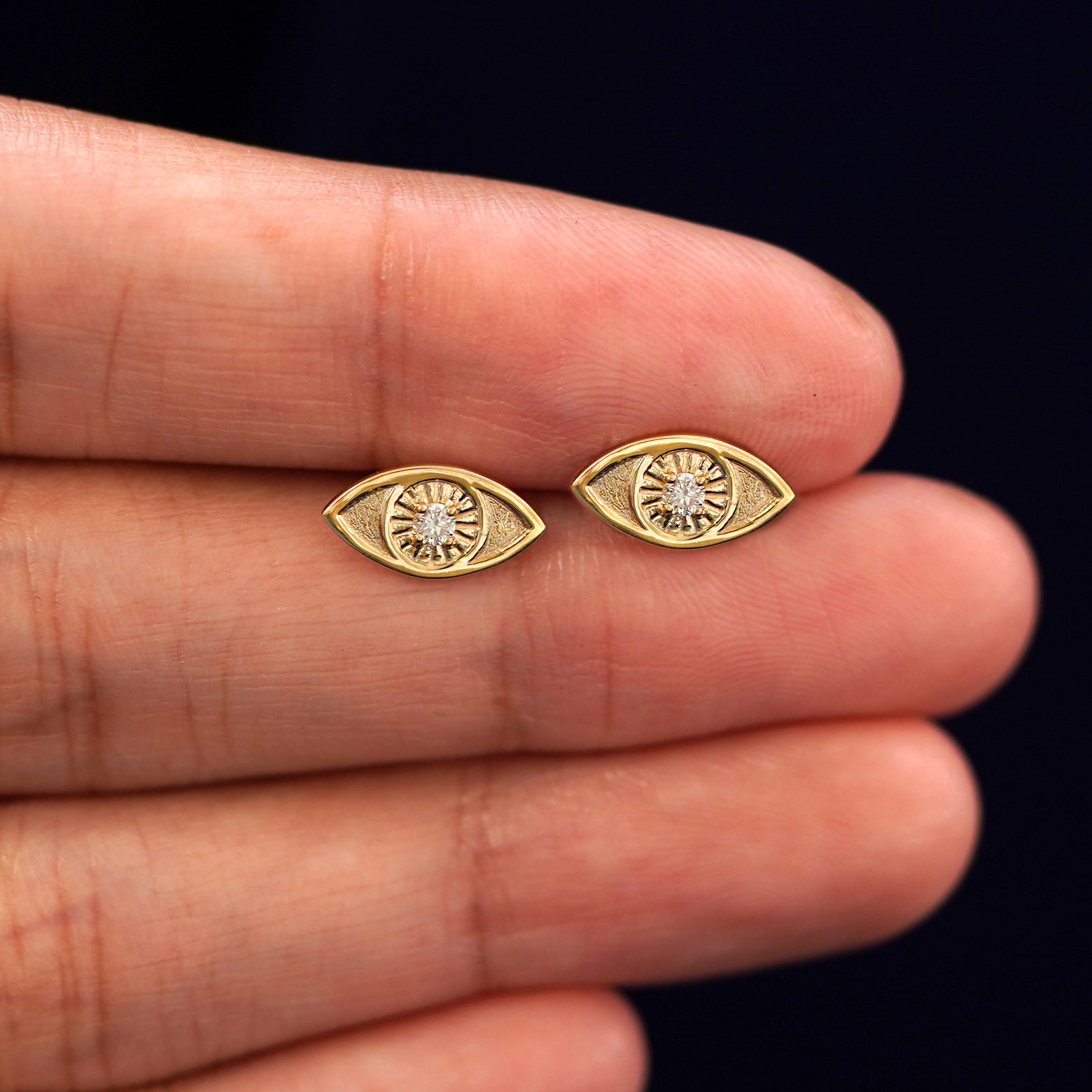 A model's hand holding a pair of recycled 14k gold Diamond Evil Eye Earrings