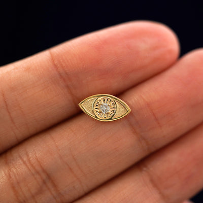 A solid 14k yellow gold Diamond Evil Eye Earring in between a model's fingers