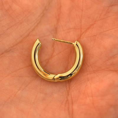 An open 14k yellow gold Chunky Oval Huggie Hoop resting in a model's palm