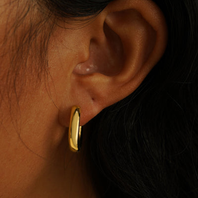 A model's ear wearing a 14 karat yellow gold Chunky Oval Huggie Hoop