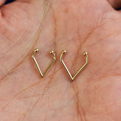 A model's palm holding two versions of the pierced Triangle Septum showing the 8mm and 10mm sizes