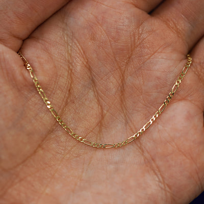 A yellow gold Figaro Bracelet resting on a model's fingers