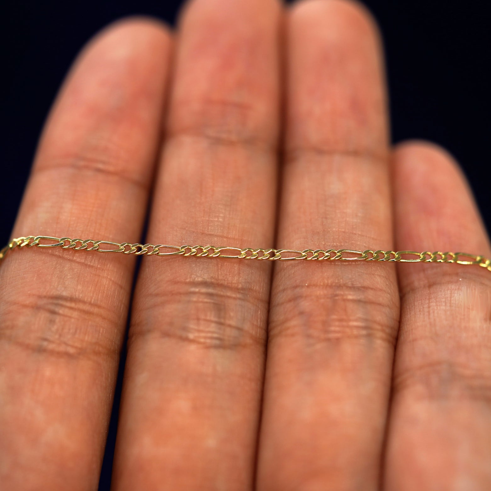 A yellow gold Figaro Bracelet draped on a model's palm
