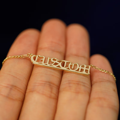 A 14k yellow gold medium custom nameplate necklace laying flat on a model's fingers to show the thickness of the letters