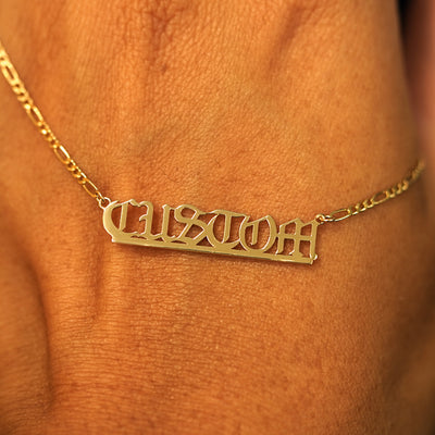 A solid yellow gold medium custom nameplate necklace draped over the back of a model's hand