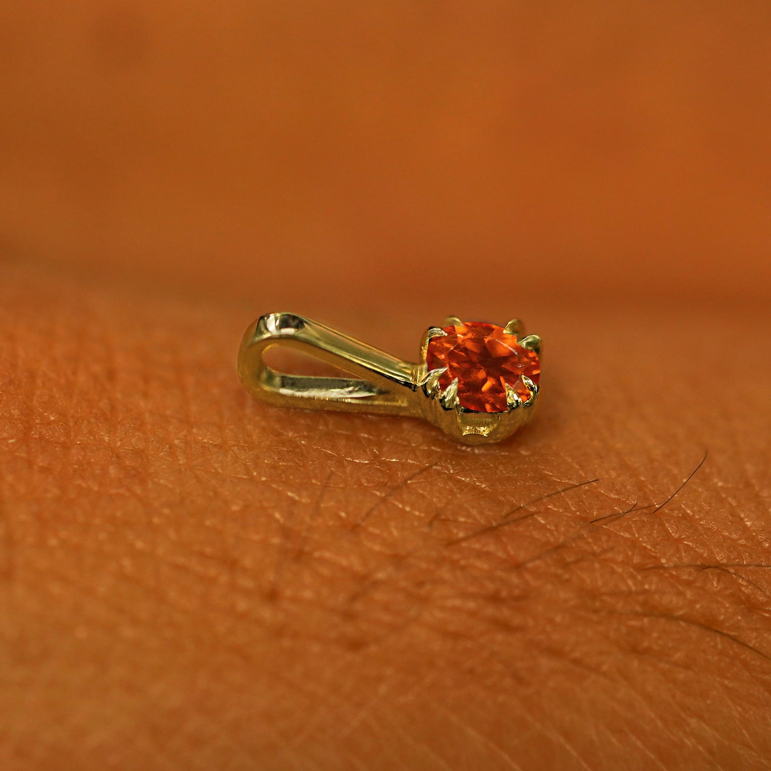 A 14k yellow gold Fire Opal Charm for chain resting on the back of a model's hand