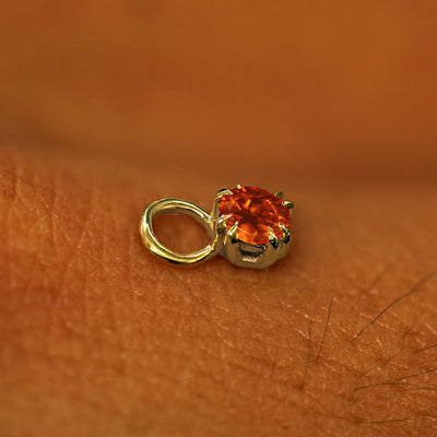 A solid yellow gold Fire Opal Charm for earring resting on the back of a model's hand