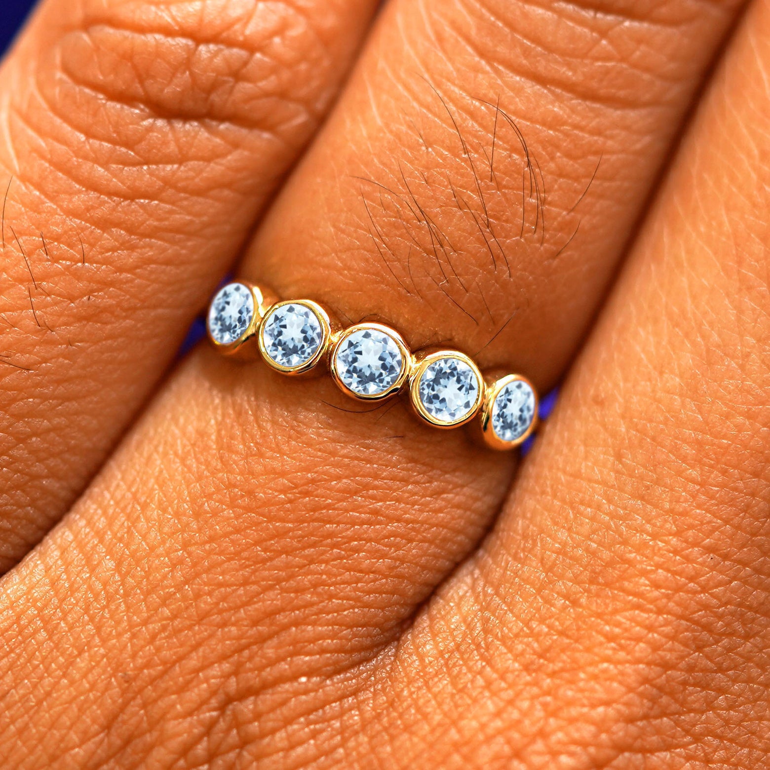 Close up view of a model's hand wearing a yellow gold 5 Gemstones Ring in aquamarine