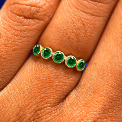 Close up view of a model's hand wearing a yellow gold 5 Gemstones Ring in emerald