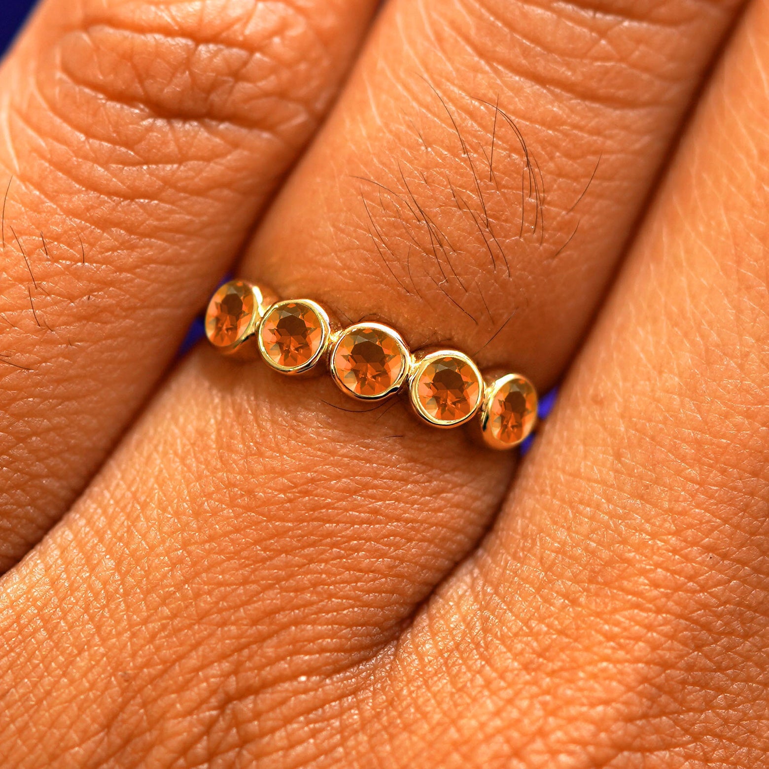 Close up view of a model's hand wearing a yellow gold 5 Gemstones Ring in fire opal
