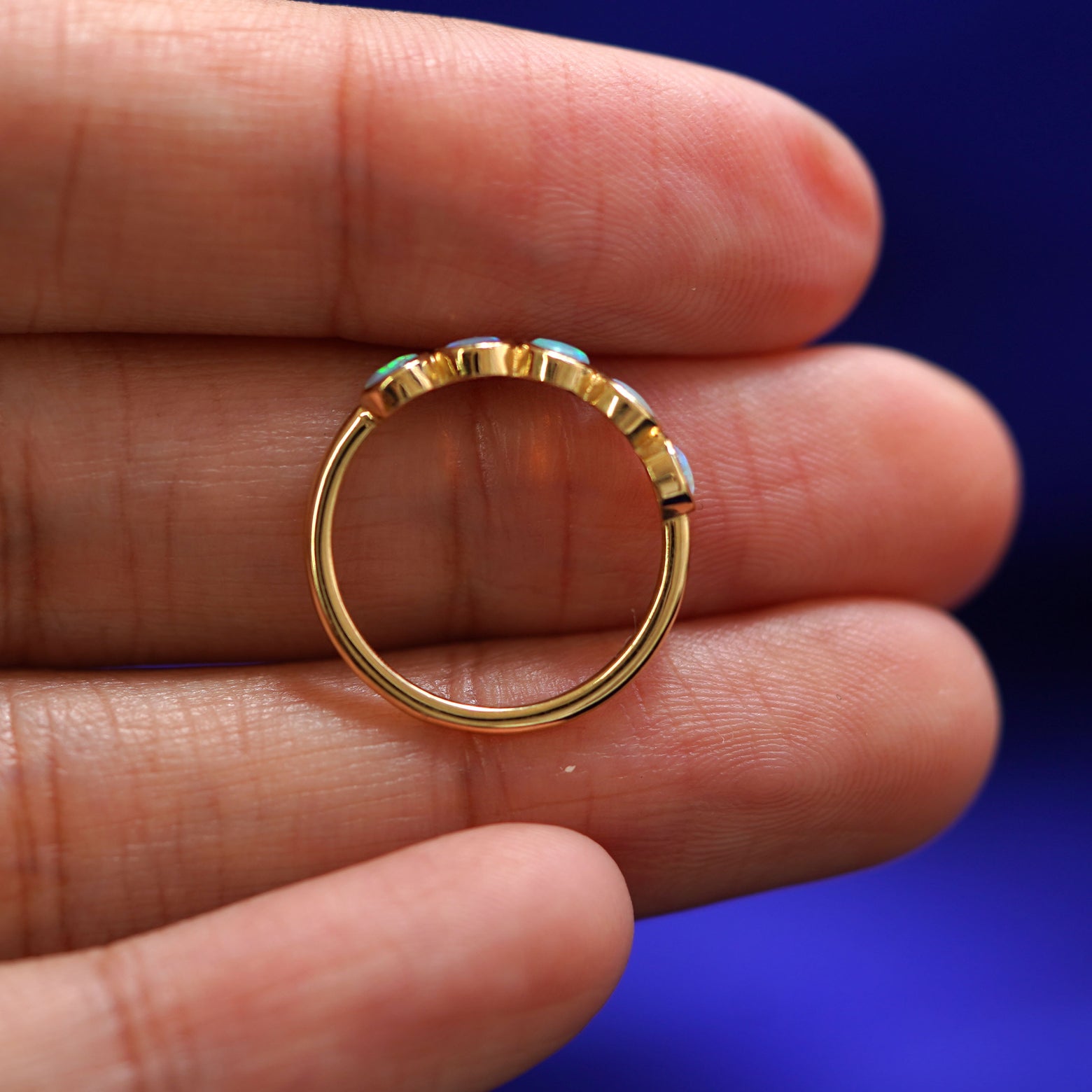 A solid gold 5 Opals Ring laying on a model's fingers to show the thickness of the band