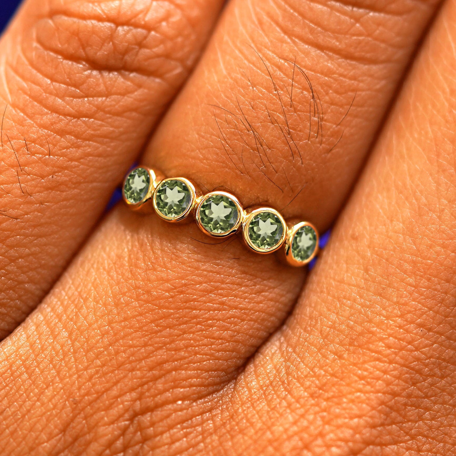 Close up view of a model's hand wearing a yellow gold 5 Gemstones Ring in peridot