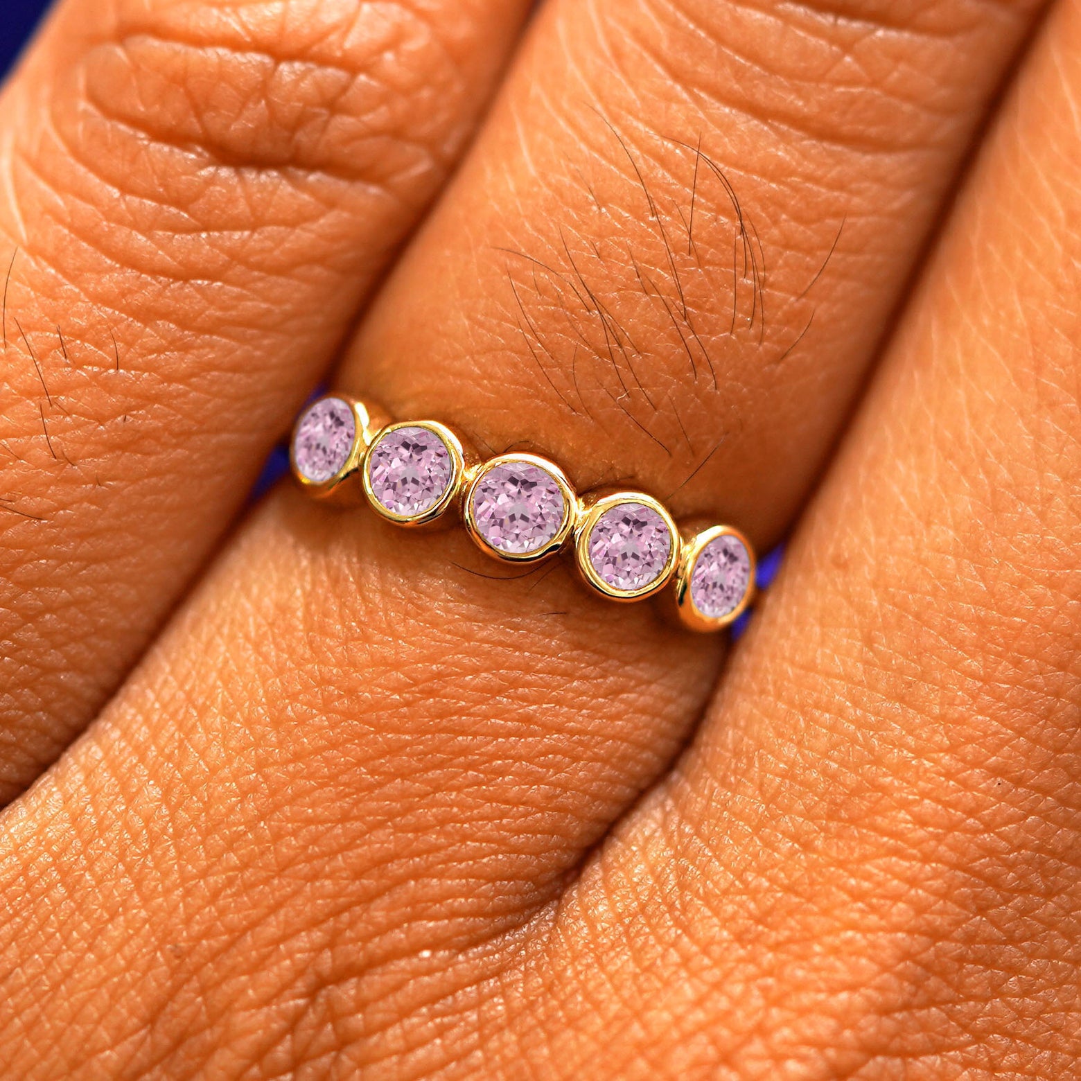 Close up view of a model's hand wearing a yellow gold 5 Gemstones Ring in pink sapphire