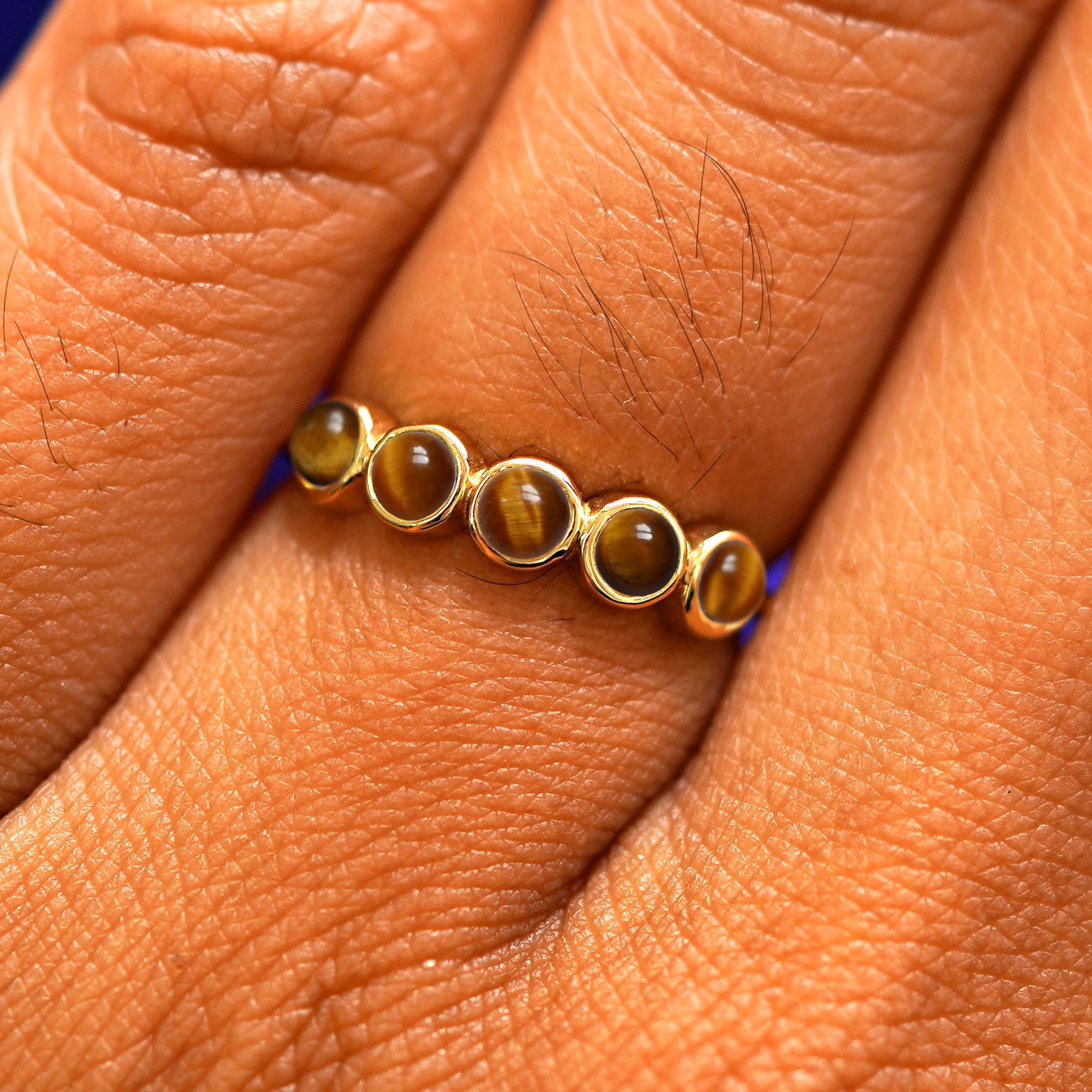 Close up view of a model's hand wearing a yellow gold 5 Gemstones Ring in tiger eye
