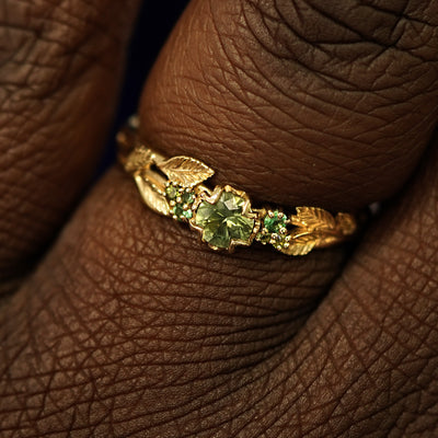 Close up view of a model's fingers wearing a 14k gold Green Sapphire Leaves and Vines Ring
