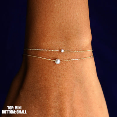 A model's wrist wearing both sizes of the Pearl Slide Bracelet layered from smallest to largest pearl
