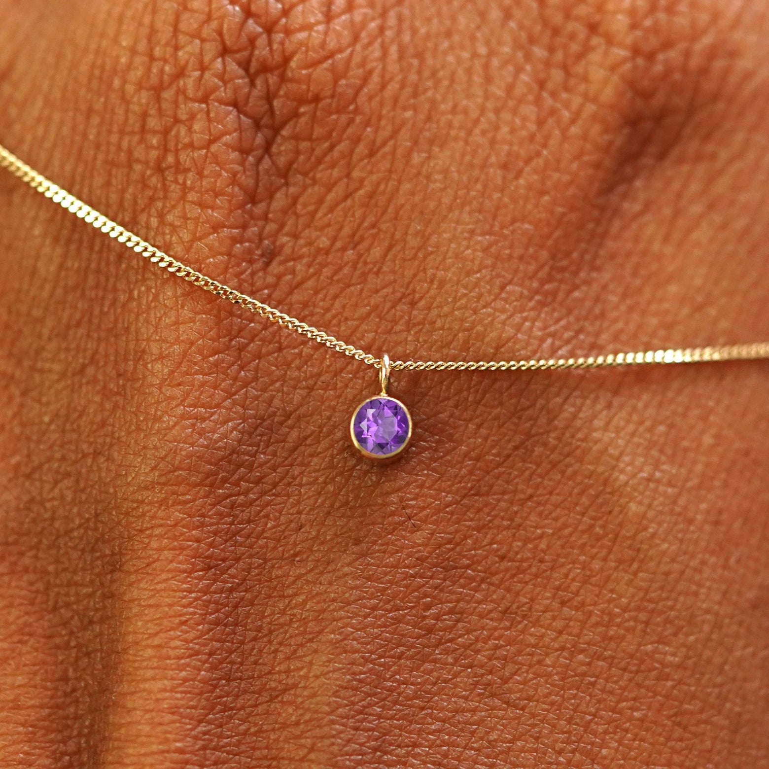 Close up view of a 14k yellow gold Amethyst Necklace draped across the back of a model's hand