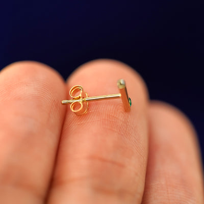 A 14k solid gold Gemstone Bar Earring laying sideways on a model's fingertips to show the post and standard backing