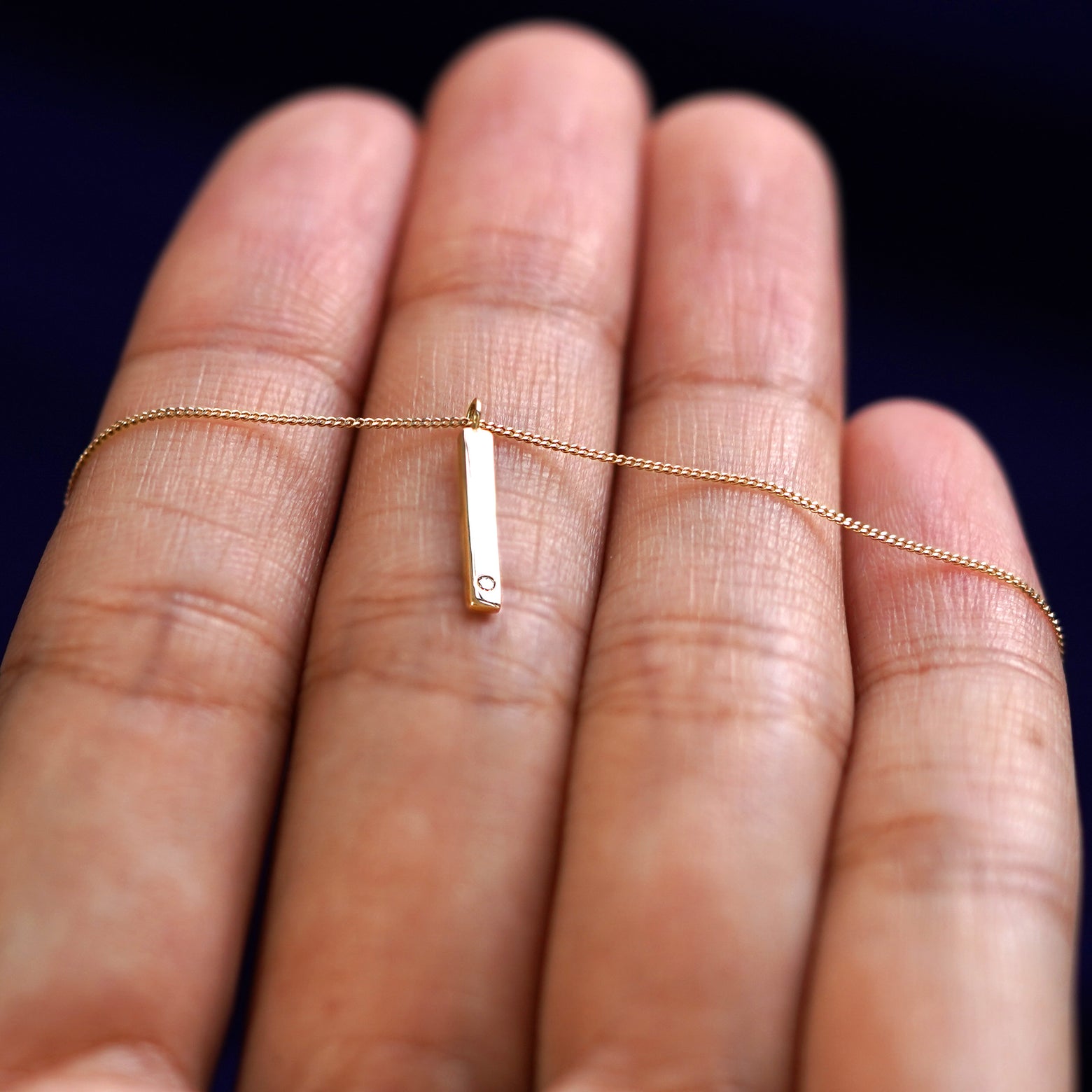 A yellow gold diamond Gemstone Bar Necklace resting on a model's fingers